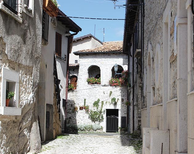 Vicolo in pietra con case fiorite nel cuore del Borgo medievale Opi: un angolo autentico tra storia e tranquillità.
