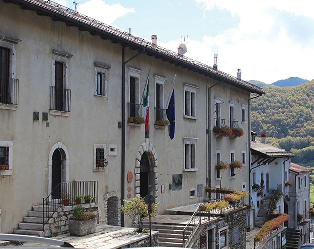 Facciata del municipio con balconi fioriti e vista sulle montagne: eleganza e autenticità nel cuore del Borgo medievale Opi.