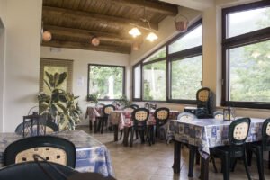 Sala da pranzo con grandi vetrate sul verde e tovaglie colorate: semplicità e bellezza al Ristorante campeggio Abruzzo.